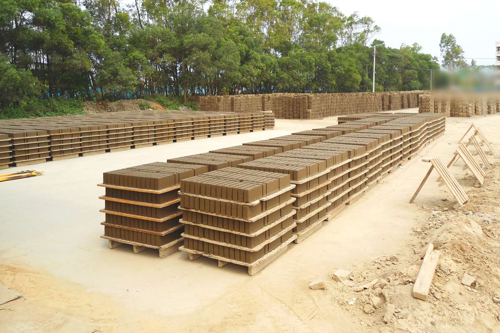 Palés de bloques de hormigón alineados en un patio de almacenamiento al aire libre, con caballetes de madera y pilas de bloques al fondo